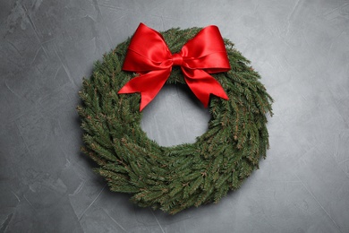 Christmas wreath made of fir branches with red bow on grey background, top view