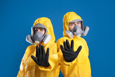 Man and woman in chemical protective suits making stop gesture on blue background. Virus research