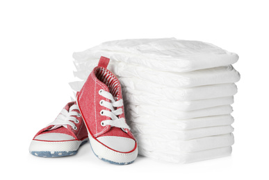 Stack of disposable diapers and child's shoes on white background