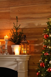 Small potted fir, candles and decor elements on white mantel near wooden wall