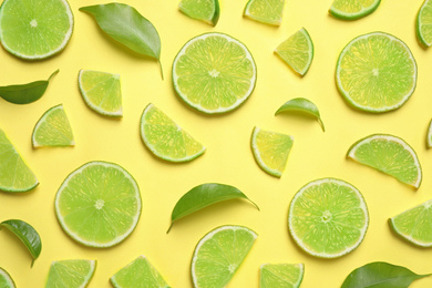 Juicy fresh lime slices and green leaves on yellow background, flat lay