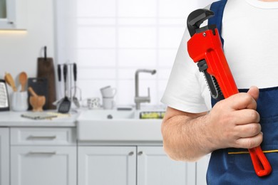 Plumber with pipe wrench in kitchen, closeup. Space for text