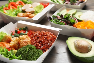Different healthy meals in takeaway boxes on wooden table, closeup. Food delivery