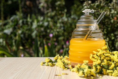 Delicious fresh honey and beautiful flowers on wooden table in garden, space for text