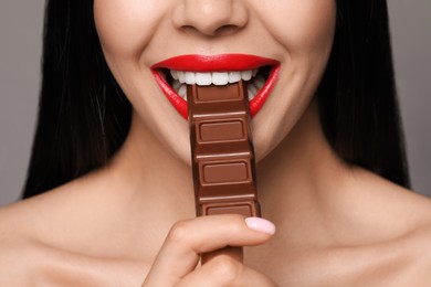 Young woman with red lips eating chocolate on grey background, closeup