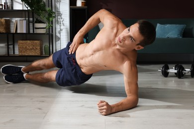 Handsome man doing side plank exercise on floor at home