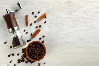 Modern manual coffee grinder with beans and cinnamon on white wooden table, flat lay. Space for text