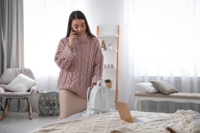 Photo of Young woman with smartphone and backpack in bedroom. Morning routine