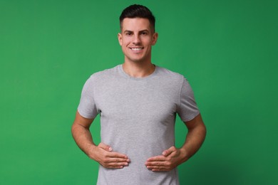 Handsome man holding hands near stomach on green background