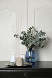 Eucalyptus branches and burning candles on black table