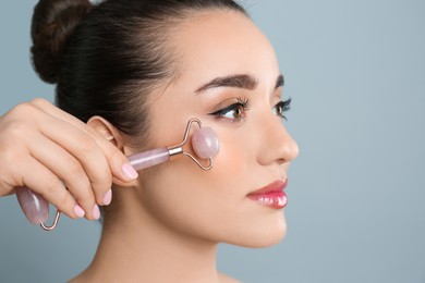 Photo of Woman using natural pink quartz face roller on grey background, closeup. Space for text
