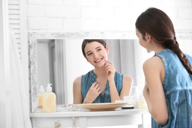 Teenage girl with acne problem looking in mirror indoors