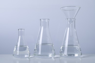 Conical flasks with transparent liquid and funnel on table against light background
