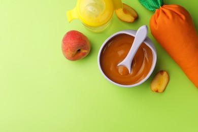 Healthy baby food in bowl and fresh peaches on light green background, flat lay. Space for text
