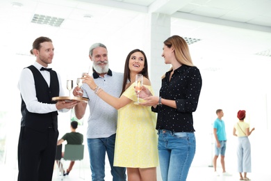 Waiter serving champagne to group of people at exhibition in art gallery