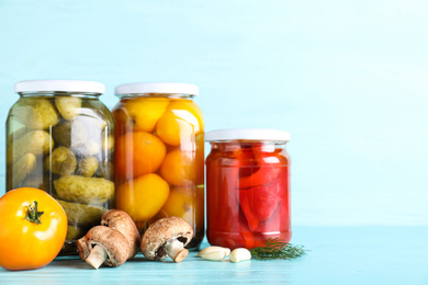 Glass jars with different pickled vegetables on light blue wooden table. Space for text