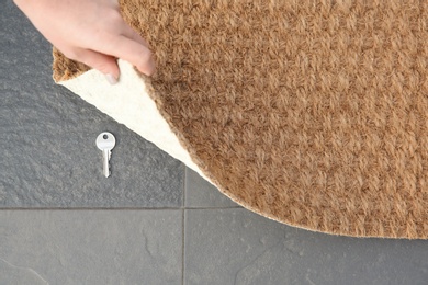 Young woman revealing hidden key under door mat, top view with space for text