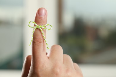 Photo of Man showing index finger with tied bow as reminder on blurred background, closeup