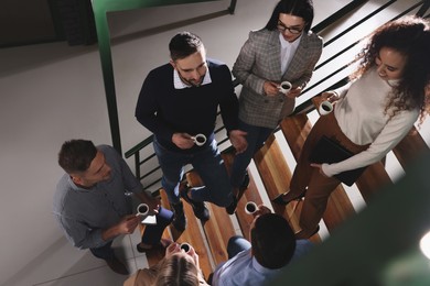 Group of coworkers talking during coffee break on stairs in office, above view