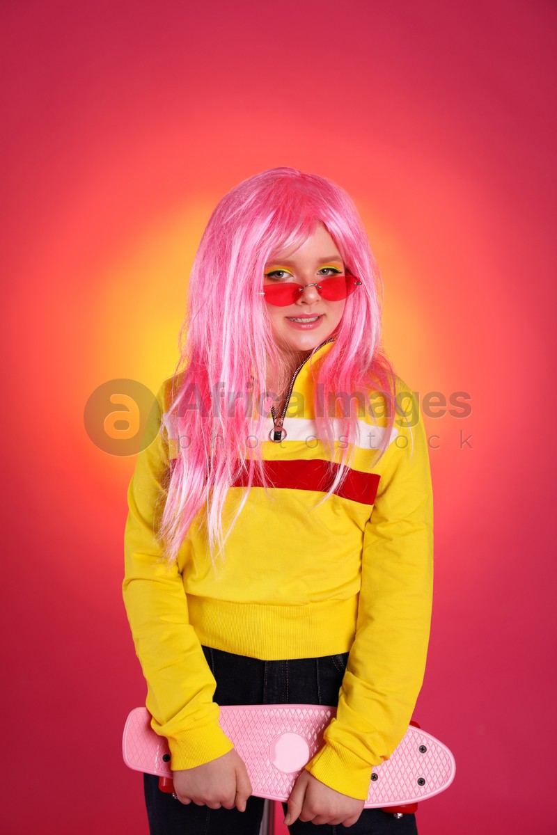 Cute indie girl with sunglasses and penny board on bright pink background