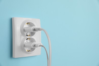 Charger adapters plugged into power sockets on light blue wall, space for text. Electrical supply