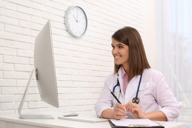 Pediatrician consulting patient online at table in clinic