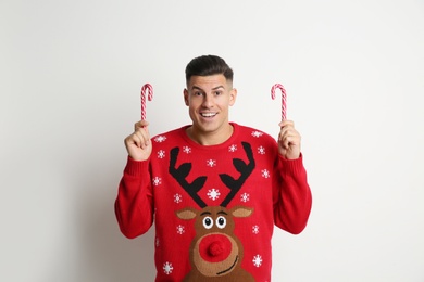 Happy man in Christmas sweater with candy canes on white background