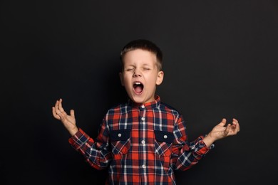Photo of Angry little boy screaming on black background. Aggressive behavior