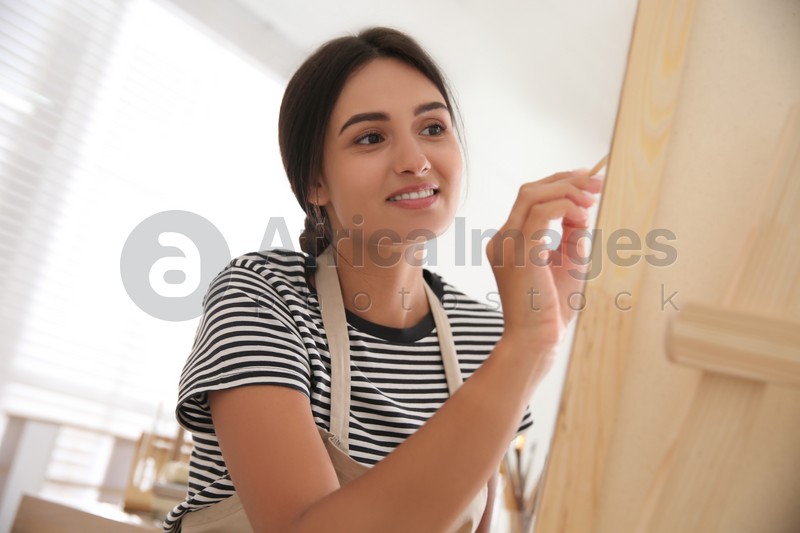 Young woman drawing on canvas with brush indoors