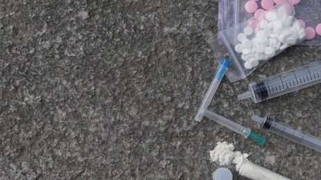 Photo of Pills, syringes and powder on stone surface, flat lay with space for text. Hard drugs