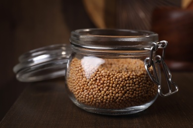 Mustard seeds in glass jar on wooden table, closeup