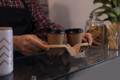Barista putting takeaway coffee cups with cardboard holder on glass table in cafe, closeup