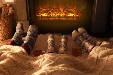 Photo of Family in warm socks resting near fireplace at home, closeup of legs