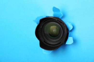 Hidden camera lens through torn hole in light blue paper