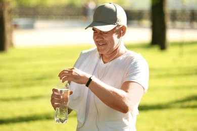 Mature man opening bottle of water after training in park