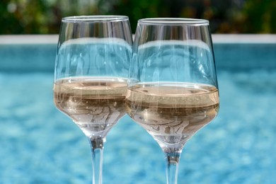 Photo of Glasses of tasty wine near swimming pool, closeup