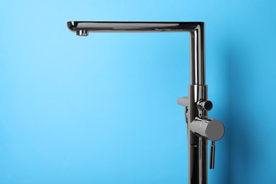 Modern single handle bathtub faucet on light blue background. Space for text