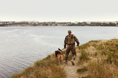Image of Man in military uniform with German shepherd dog near river