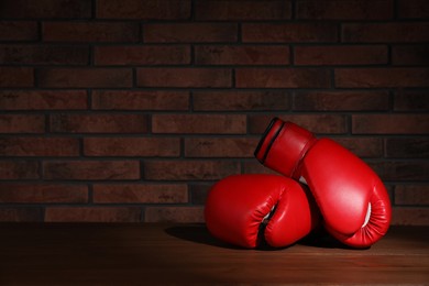 Pair of red boxing gloves on wooden table near brick wall