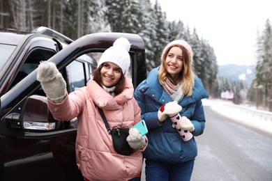 Friends standing near car on road. Winter vacation