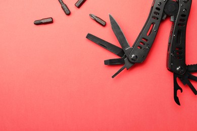 Compact portable black multitool and details on red background, flat lay. Space for text
