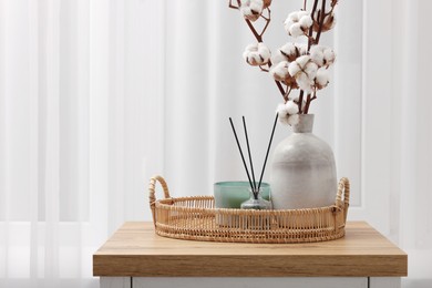 Candle, reed diffuser and vase with cotton branches on wooden commode indoors. Space for text