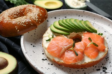 Photo of Delicious bagel with cream cheese, salmon and avocado on plate, closeup