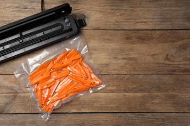 Vacuum packing sealer and plastic bag with cut carrots on wooden table, flat lay. Space for text