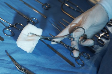 Doctor holding medical clamps with pad near table of different surgical instruments indoors, closeup