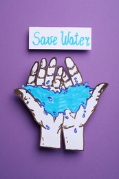 Save water concept. Hands with water paper figure near card on violet background, top view