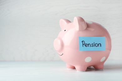 Piggy bank and paper with word PENSION on table. Space for text