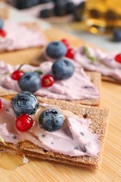 Tasty cracker sandwiches with cream cheese, blueberries, red currants and honey on wooden board, closeup