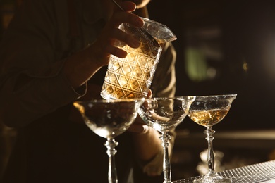 Barman pouring cold martini into glasses on counter, closeup
