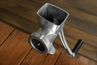 Photo of Metal manual meat grinder on wooden table, closeup